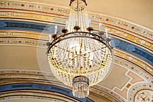 Antique chandelier with crystal trimmings and candles under the painted ceiling.