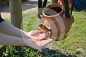 Antique clay washbasin for washing hands pours water on women's hands.