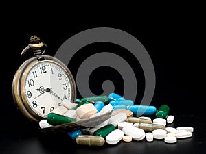 Antique clock on multicolored of drug and capsule is on the black background. Close up. We are against drugs anti drugs, cure in