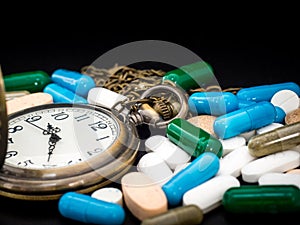 Antique clock on multicolored of drug and capsule is on the black background. Close up. We are against drugs anti drugs, cure in