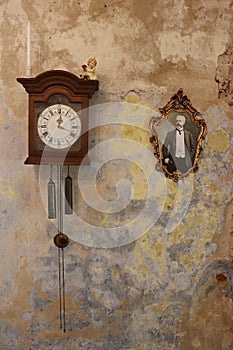 An antique clock with weights and a very old framed photograph of a man on the wall