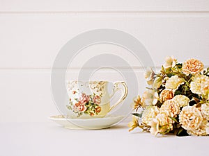 Antique cup of tea with saucer ,yellow orange rose flowers background