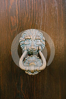 Antique door handle on a wooden brown door in the form of a beast`s face with a knock ring in the mouth.