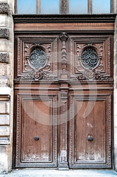 Antique double door gate with of aged ornate carving fretwork wooden panels and door windows of building in Paris France.