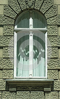 Antique Eastern Europe building has old wood framed keyhole window & decoration in plaster surrounding window frame. See cherub at