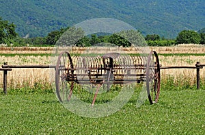 Antique farm equipment, a hay rake machinery, on grass in front of a wheat field