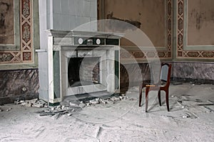 An antique fireplace and a chair next to it in an old abandoned manor house.