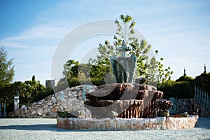 Antique fountain in the garden of the old castle. Stone walkway. Alley in beautiful garden with flowers and trees around. Summer