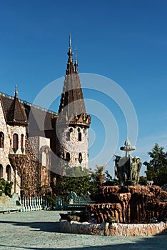 Antique fountain in the garden of the old castle. Stone walkway. Alley in beautiful garden with flowers and trees around. Summer