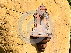 Antique French ornate wall fountain lavabo or planter with scrolling details and accents mounted in a stone block outside. A tap i photo