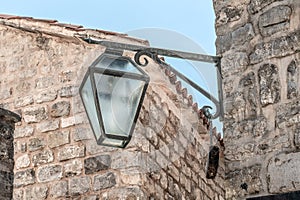 Antique glass lantern with a forged frame hangs on the corner of stone building