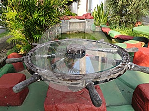 Antique glass table with old wooden frame model of a ship& x27;s rudder located in the garden