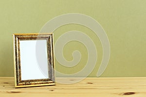 Antique golden picture frame on wooden table with khaki background