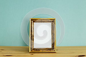 Antique golden picture frame on wooden table with mint green background