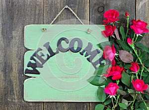 Antique green welcome sign with flower border of red roses hanging on rustic wood background