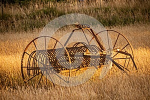 Antique hay rake in a farmers field during a golden sunset.