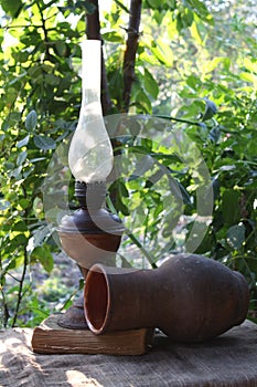 Antique lamp jug and an old book on the background of the garden