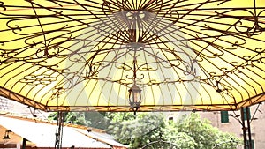 An antique lantern on the ceiling of a wrought-iron gazebo with a yellow roof.
