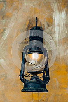 Antique lantern hanging against wall. Vintage lantern with a glowing bulb.