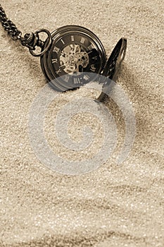 Antique old pocket fob watch with chain partly buried in sand.