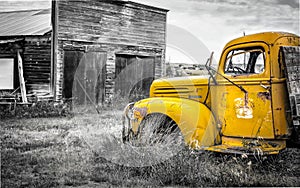 Antique old truck with yellow cab sitting by an old garage.