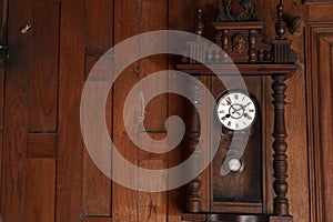 Antique pendulum clock hanging on the wooden wall