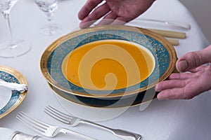 Antique plate filled with carrot soup being served on elegant table set with beautiful antique silverware