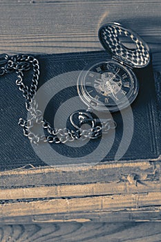 Antique pocket fob watch with a chain on a stack of old books.  On a wooden background