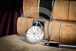 Antique pocket watch on burled wood with old leather bound books and fountain pen