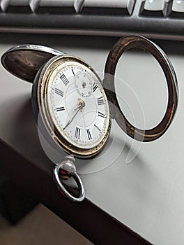 Antique pocket watch on a gray table, with a computer keyboard next to it