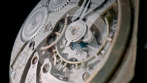 Antique pocket watch mechanism isolated on black studio background. Macro shot of clockwork of stopped clock with spring