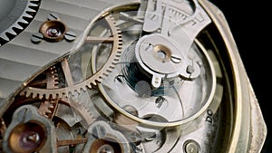 Antique pocket watch mechanism moving on isolated black studio background. Macro shot of clockwork with rotating spring