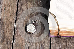 An antique pocket watch and an old book on an old wooden table