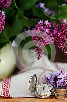 Antique pocket watch on a wooden background, with lilac flowers