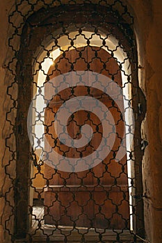 Antique portal in church. Entrance with iron grating in castle. Vintage wooden door with grating. Cell in medieval temple.