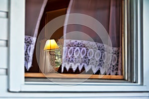 Antique reading lamp seen through a window with curtains blowing