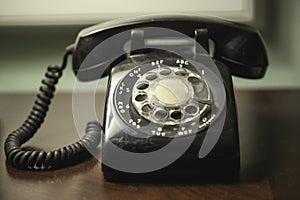 Antique retro vintage black rotary telephone with coiled cord on a wood desk