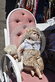 Antique Saturday market in old quarter. Vintage shabby doll sits on a tattered armchair on a sunny