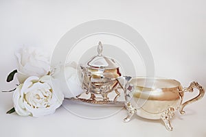 Antique silver creamer and sugar set and decorative white flowers in white background. Afternoon tea concept.