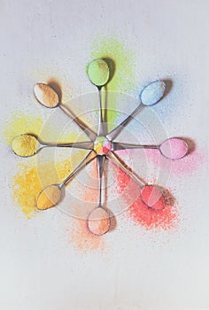 Antique silver spoons laid out in patterns holding brightly rainbow colored jello powder, on a textured background