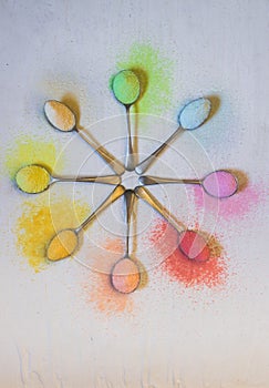 Antique silver spoons laid out in patterns holding brightly rainbow colored jello powder, on a textured background