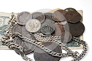 Antique silverware, silver and bronze coins and jewelry lying on old banknotes