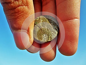 Antique stone coin in hand on blue