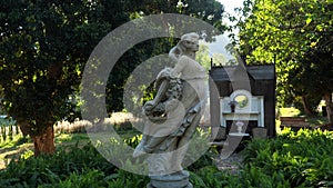 Antique stone female statue in garden in sunlight. Ancient sculpture of woman in dress with flowers. Marble statue in a