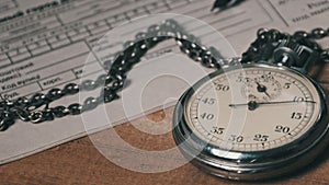 Antique Stopwatch Lies on Wooden Desk with Old Documents and Counts Seconds