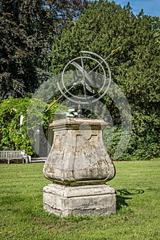 Antique sun dial in a garden, with grass and trees