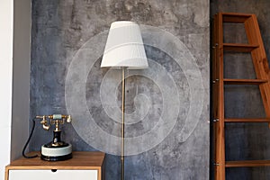 Antique telephone and white floor lamp on the background of a concrete wall and a wooden staircase, ideal for reading in