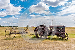 Antique tractor pulling a hay rake with St. Anthony Roman Catholic Church in Illerbrun, SK in the backg