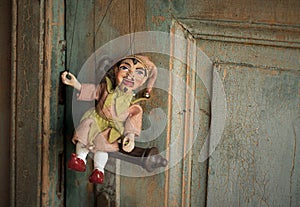 An Antique Traditional Puppet Laughing And Sitting On The Handle Of The Very Old Door