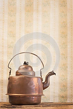 Antique vintage copper kettle on the background of old wallpaper